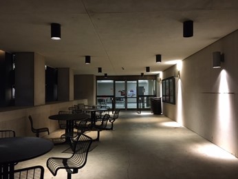 A set of doors on the exterior of the Wells Library. The doors are at the end of a patio, with several sets of tables and chairs on the left side leading up to the doors.